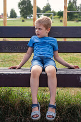 Lonely bored boy sitting on bench. Sad mood in child depression concept