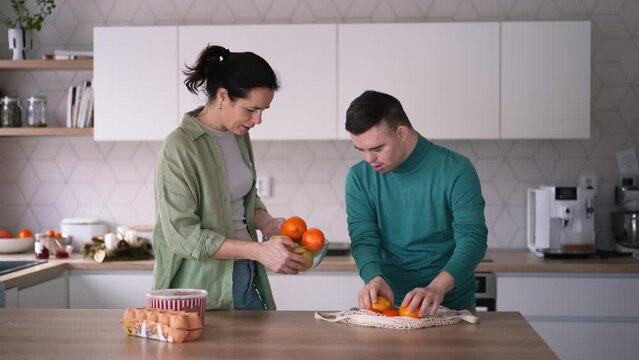 Young man with Down syndrome preparing breakfast with his mother at home. Morning routine for man with Down syndrome.