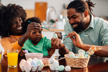 Jolly african american family is coloring easter egg together at home.