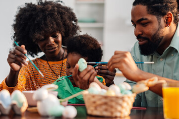 Young multicultural parents are painting easter eggs with toddler.