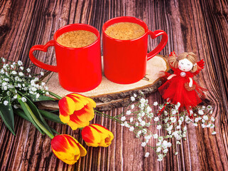 Two red coffee cups with hearts, a fairy doll, a bouquet of red tulips and gypsophila flowers on a...