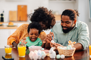 An interracial family is having fun painting easter eggs at home.