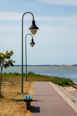Pedestrian path with a bench for rest and beautiful two street lights by the shore of a small sea port in Kintai, Lithuania