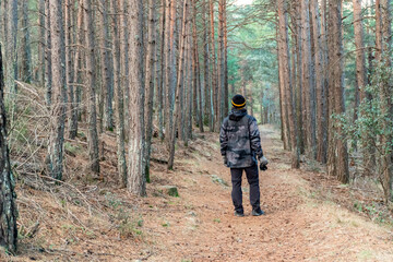 Rear view of a man walking through the forest, wearing a camouflage raincoat and wool hat.