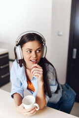Young woman enjoying music and coffee at home, wearing headphones and looking relaxed and beautiful in cozy setting