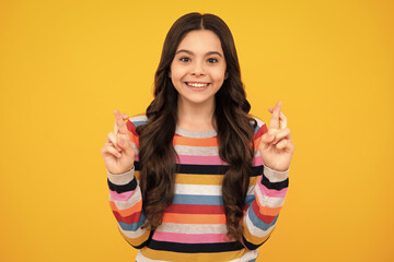 Teenager child girl crossing her fingers and wishing for good luck, isolated on yellow studio...