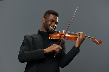 Talented young African American man playing the violin with passion on a neutral gray background