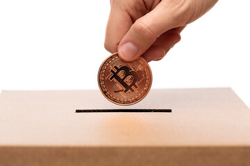 charity, cryptocurrency and fundraising concept - close up of hand putting bitcoin into donation box