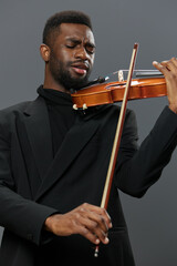 Elegant African American man in black suit playing violin on gray background in studio setting