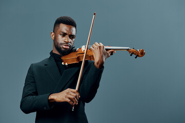 Talented African American man in a suit playing the violin against a neutral gray background © SHOTPRIME STUDIO