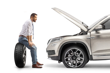 Profile shot of a pensive man sitting on a tire in front of his vehcile with open hood