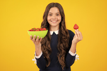 Teen girl tasting a strawberry, child with strawberry bowl on yellow background. Organic...