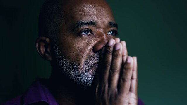 Spiritual African American senior person praying to GOD, closing eyes in contemplation with hands clenched together. Faithful man asking for HELP and SUPPORT