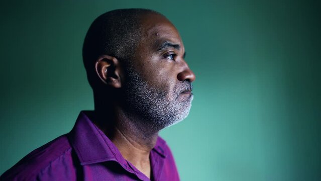 One pensive senior black man regretting past decision grimacing during challenging times standing indoors in isolation gazing at window, profile close-up face