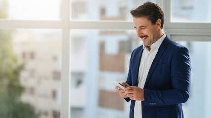 Smiling businessman in a blue suit checking his phone in a well-lit office space