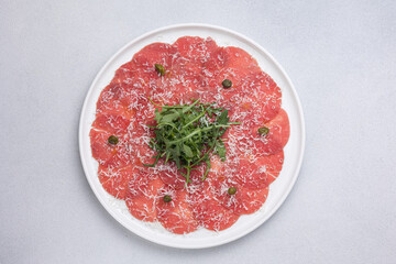 Fresh carpaccio with veal and arugula on a round plate