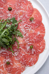 Fresh carpaccio with veal and arugula on a round plate