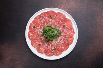Fresh carpaccio with veal and arugula on a round plate