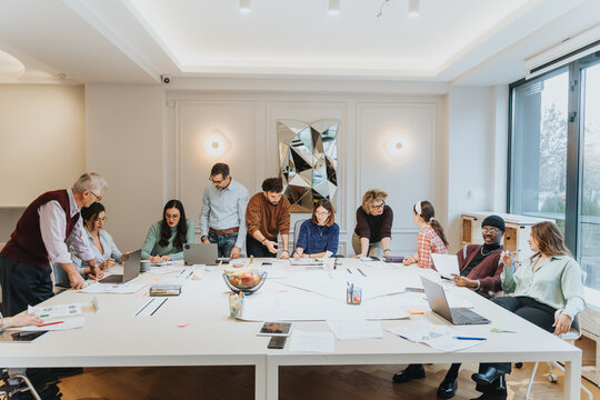 A dynamic business meeting in progress with a group of people collaborating and brainstorming ideas around a large table in a bright, modern office environment.