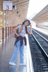 Fototapeta premium Rear view of a young woman with backpack standing on a train station, travel concept, Portrait of Asian woman tourist waiting for the train at railway station
