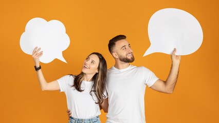 A man and woman holding blank speech bubbles overhead, looking at each other with smiles