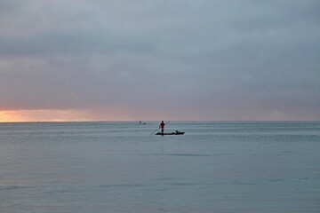 A fisherman over a raft in the wide sea water. Early morning day, first sun light. All blue water and sky