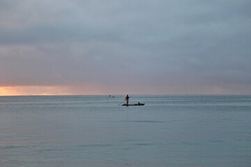 Fototapeta premium A fisherman over a raft in the wide sea water. Early morning day, first sun light. All blue water and sky