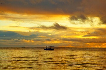 Sunrise golden light all around. Reflections on sky, sea water. Small fishierman boar anchored   close to water edge. Japaratinga, Alagoas, brazil
