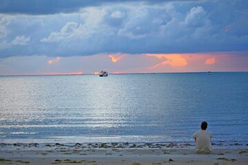 Blue sunrise on Japaratinga beach, Alagoas, Brazil. Cloudy sky, calm sea waters, stripe orang01014e on horizon line, sun light reflections. Small fishing boat in horizon line