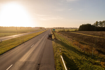 Fototapeta na wymiar Drone photography of tractor mowing grass near a highway during autumn morning