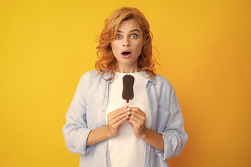 Portrait of beautiful woman eating ice cream on orange yellow background. Girl eating popsicle ice pop. Excited expression female portrait. Amazed surprised woman face.