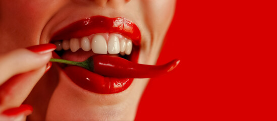 une femme met un piment rouge fort dans sa bouche et le serre entre les dents - fond rouge