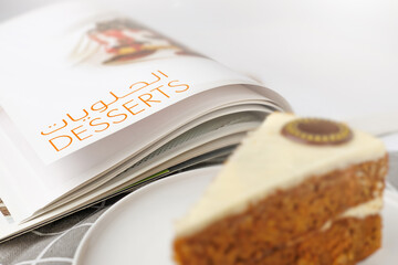 Slice of carrot cake on a white plate with a book in the background