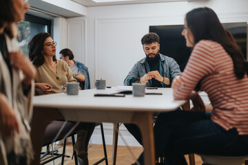 Fototapeta premium Diverse team in informal business meeting in a well-lit contemporary office. Focused colleagues discuss project strategies, fostering teamwork and collaboration.