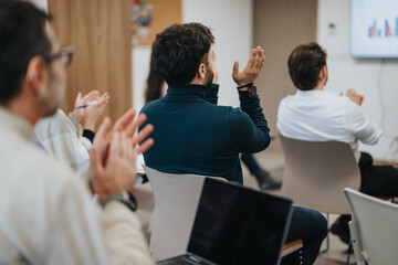 Engaged audience clapping at business presentation in modern office setting.