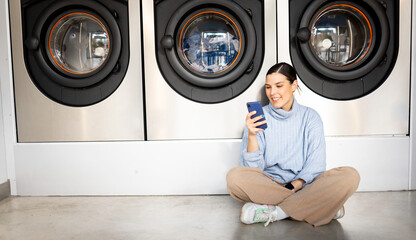 A young and pretty girl is inside a public self-service laundromat. The woman waits for her to wash...