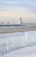 tourists view a frozen light beacon and  an icy walk on the shores of Lake Michigan