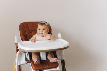 Happy little baby girl sitting in high chair in kitchen at home