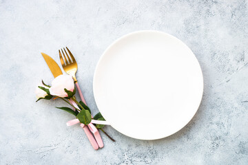 Table setting, festive table serving with white plate, modern cutlery and pink flowers. Top view at...