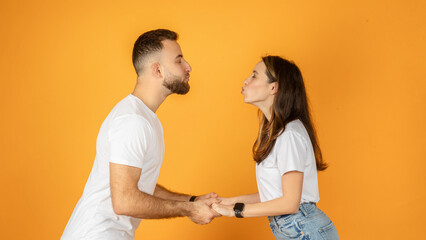 A playful young couple holding hands and puckering up as if preparing for a kiss