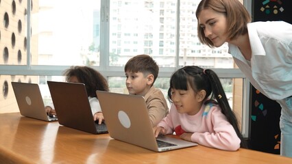 Smart teacher teaching and looking student using laptop at classroom. Professional instructor...