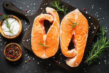 Raw salmon steaks on cutting board at black background. Top view with ingredients for cooking.