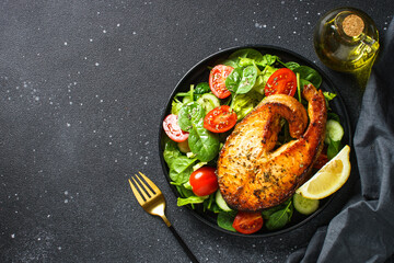 Salmon steak and fresh green salad on black background. Keto diet, healthy food. Top view copy space.