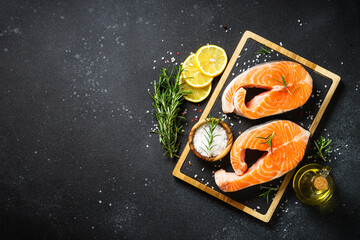 Fresh fish. Salmon steaks on cutting board at black background. Top view with ingredients for...
