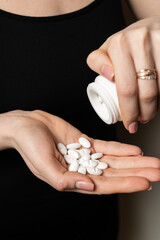 Female hands pour out handful of white pills tabs from the jar to take medication to kill pain