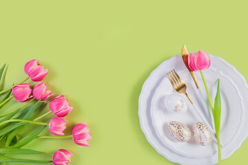 Fototapeta na wymiar Pink tulips, table place setting and festive easter decor on pastel green background. Happy easter greeting or invitation card. Top view, flat lay, copy space for text