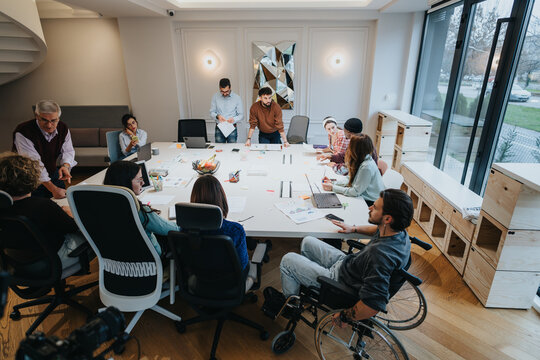 Inclusive business meeting with a diverse team engaged in discussion. A member in a wheelchair actively participating adds to the dynamic. - Powered by Adobe