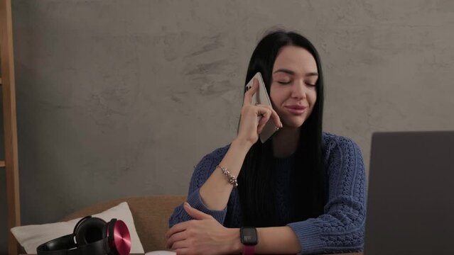 The girl is talking on the phone while sitting at the laptop in the room