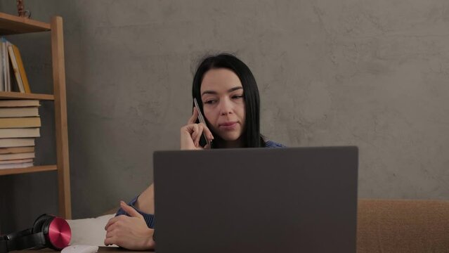 The girl is talking on the phone while sitting at the laptop in the room