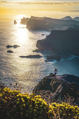Female tourist walks along steep cliff overlooking the sea and rugged foothills of Madeira's...
